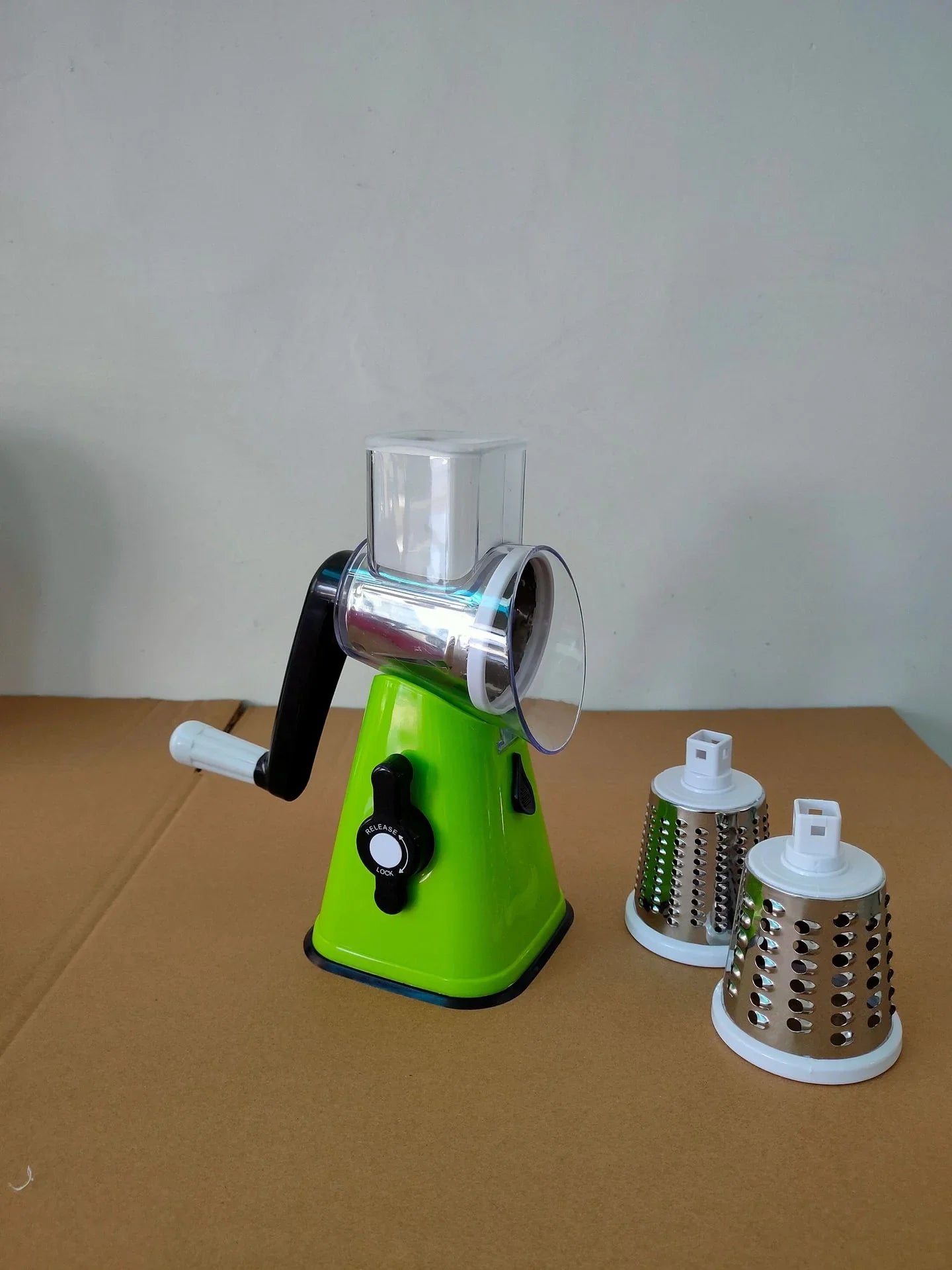 Green manual grinder with three attachments on a brown surface