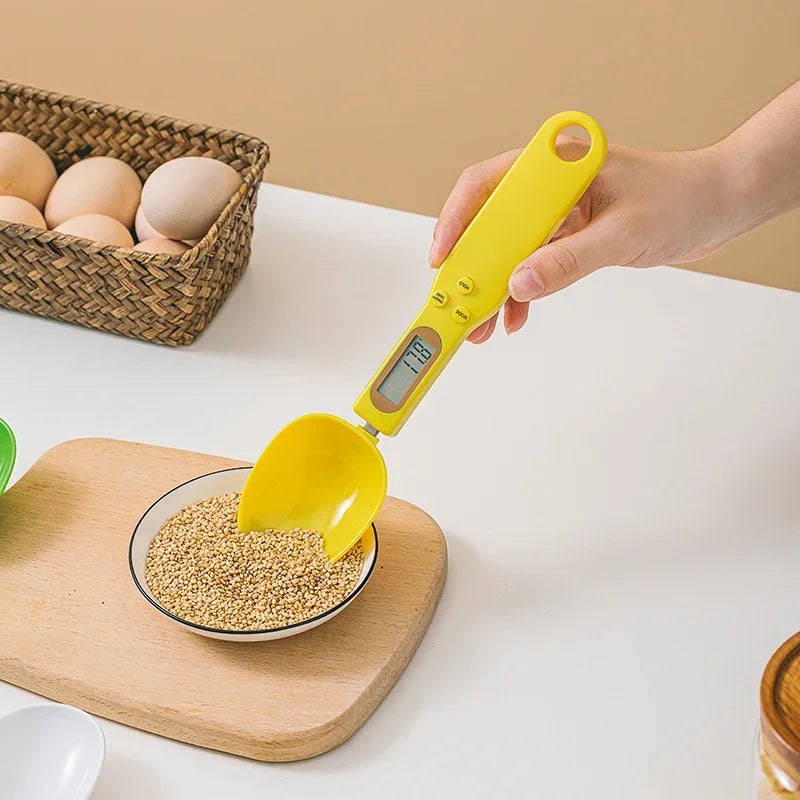 Yellow digital measuring spoon being used to measure grains on a white surface with a basket of eggs in the background.
