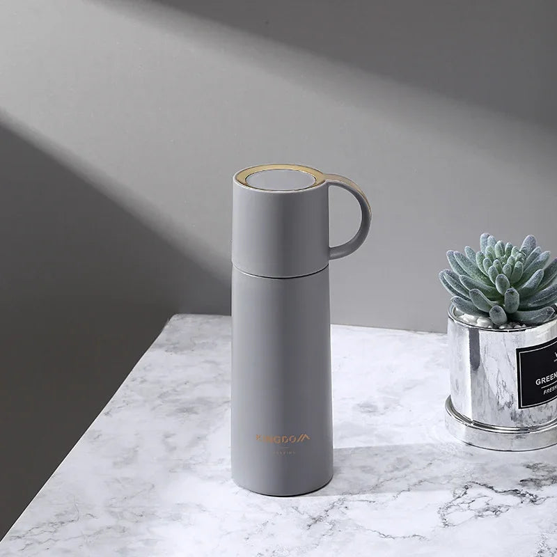 Gray thermos bottle on a marble surface with a small plant in the background