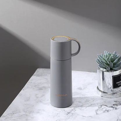 Gray thermos bottle on a marble surface with a small plant in the background
