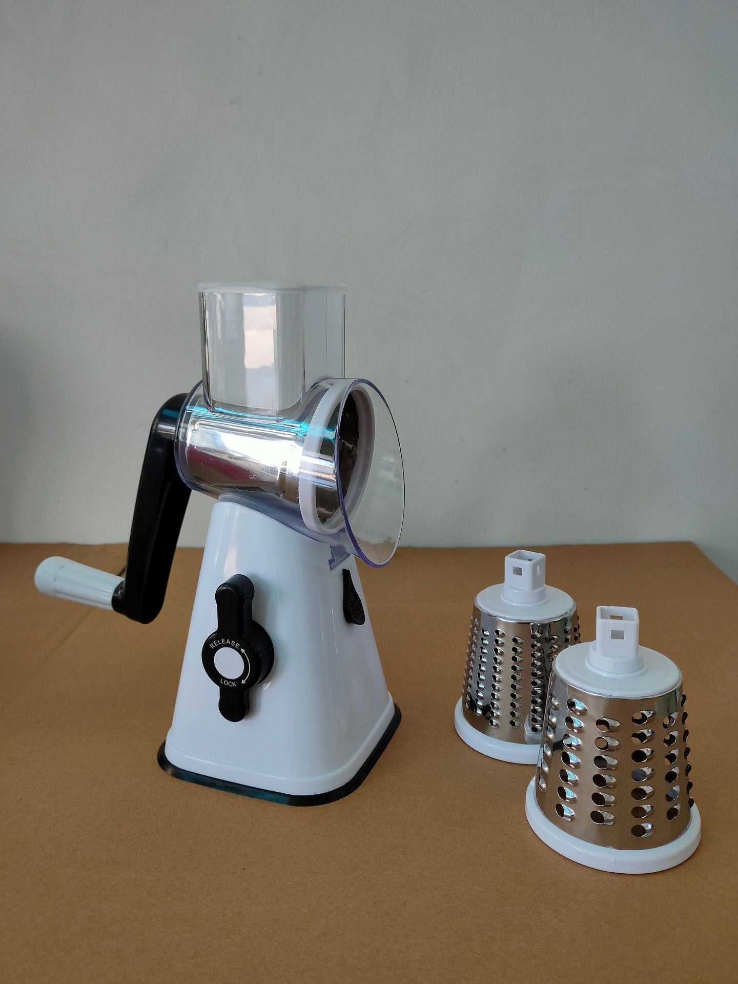 Manual rotary cheese grater with three different grating heads on a brown surface.